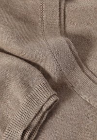 Pull beige en maille avec un col rond, des poignets côtelés et un tissu texturé. Gros plan montrant un motif de maille fin et une apparence douce et chaleureuse.