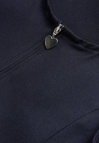 Marine kleding met een gladde textuur heeft een ritssluiting, geaccentueerd door een kleine hartvormige zilveren ritslepel.