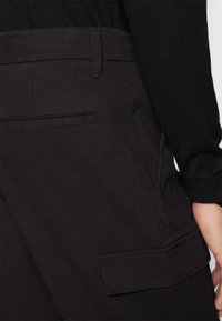 Pantalones cargo negros con grandes bolsillos laterales y un bolsillo trasero plano. El material es suave, con una textura lisa y detalles de costura limpios.