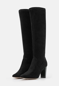 Botas negras de ante altas hasta la rodilla con punta afilada y tacón grueso. Presentan una textura suave y un detalle de costura mínima.