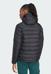 Chaqueta acolchada negra con capucha, que presenta secciones acolchadas y una textura suave. El diseño incluye un cuello alto y puños elásticos.