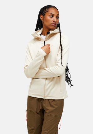 Lichtbeige fleecjack met een hoge kraag, een ritssluiting aan de voorkant en met rits afgesloten zakken. Gladde textuur met een aangesloten ontwerp, gedragen over een paar bruine broek.