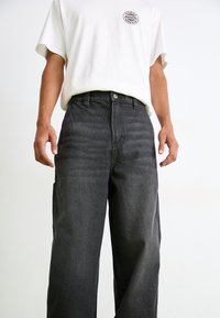 Grå denim-bukser med en avslappet passform, med knappelukking foran, beltehemper og sidelommer. Materialet har en lett tekstur.