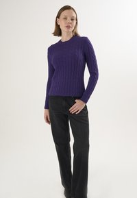 Lila Kabelstrickpullover mit langen Ärmeln, rundem Halsausschnitt und gerippten Bündchen, kombiniert mit schwarzen geraden Jeans. Glatte Textur.