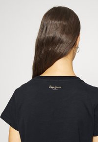 Svart bomullströja med korta ärmar, med en liten guldig logotyp på baksidan. Slät textur och klassisk rundad halsdesign.