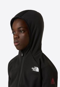 Fekete cipzáras kapucnis pulóver, sima anyagból készült. Szűk szabású kapucnival, fehér logóval a mellkason és piros részletekkel az ujján.