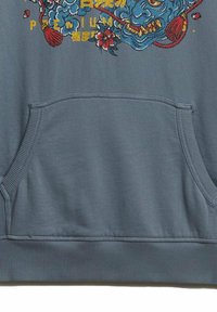 Sudadera de color azul claro con un bolsillo canguro en el frente, que presenta diseños bordados coloridos de una cara, patrones florales y texto.