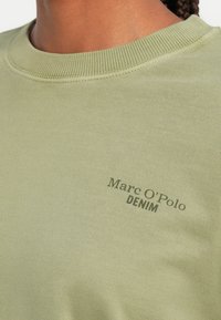 Svetlozelená mikina s rebrovaným okrúhlym výstrihom, mäkká na dotyk, s malou potlačou loga "Marc O'Polo DENIM" v tmavozelenej farbe.