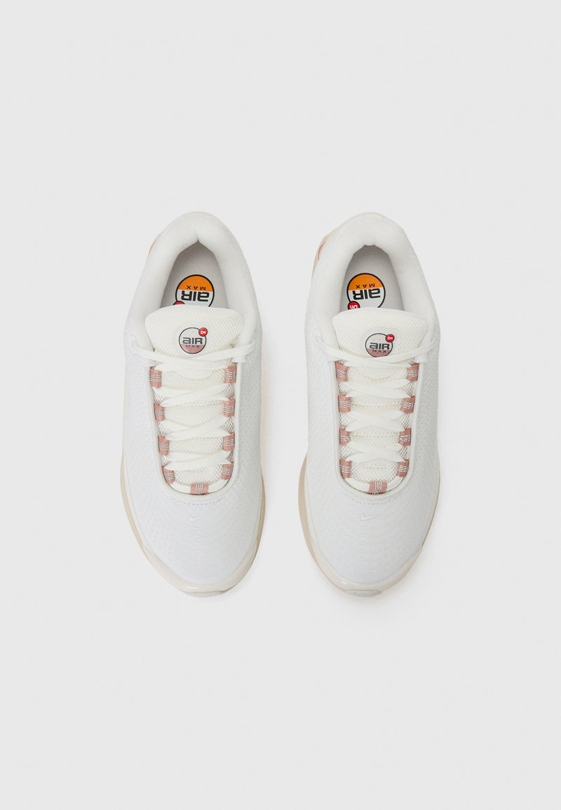 Baskets blanches avec une tige en mesh texturé, accents roses sur les lacets et un logo Air Max visible sur la languette. Semelle en caoutchouc légèrement courbée.