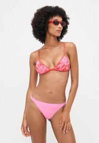 Rosa bikini med en teksturert blomstermønstrete bralette med kontrasterende stropper og solide ribbestrikkede lavt-røykede bunn. Gummierte røde solbriller.