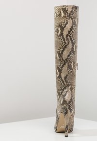 Knee-high, snake-print boot in shades of beige and brown, made from textured material, featuring a pointed toe and stiletto heel.