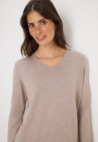 Pull long à manches longues beige clair avec un décolleté en V. Texture douce et tricot lisse, avec un design simple et classique sans motifs ni embellissements.