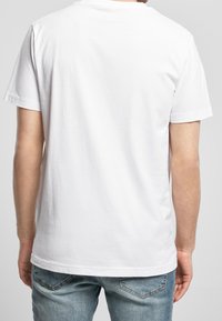 Wit katoenen T-shirt met een ronde halslijn, korte mouwen en een effen ontwerp, gedragen met lichtblauwe spijkerbroek, bekeken vanaf de achterkant.