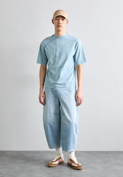 Chemise en denim bleu clair à manches courtes avec des coutures contrastantes, associée à un pantalon en denim bleu clair ample. Baskets marron et rose.