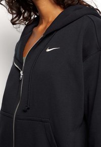 Black zip-up hoodie made of soft fabric, featuring a silver Nike logo on the chest, a drawstring hood, and front pockets.