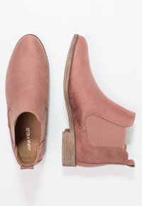 Botas Chelsea de ante rosa con paneles laterales elásticos, tacones de madera apilados y tiradores, mostradas desde vistas superior y lateral sobre fondo blanco.