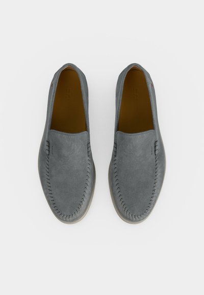 Ζευγάρι γκρίζα μοκασίνια από σουέτ ύφασμα τύπου slip-on, με εμφανείς ραφές γύρω από τη μύτη, από πάνω σε λευκό φόντο.
