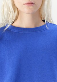 Blå bomullssweatshirt med rund hals, med en jevn tekstur og ensfarget design. Ingen mønstre eller aksenter er synlige.