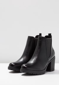 Schwarze Stiefeletten mit einem glatten Lederobermaterial, elastischen Seitenpaneelen, einem klobigen Absatz und einer strukturierten Gummisohle für besseren Halt.