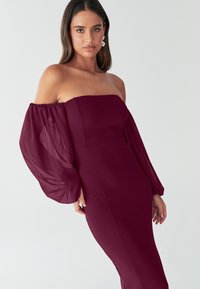 Bordo obleko brez naramnic z prozornimi, napihnjenimi rokavi. Gladek, oprijet zgornji del s strukturiranim dizajnom, ki poudarja elegantno krojenje.