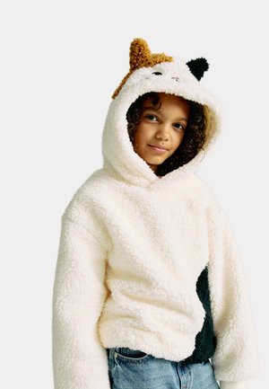 Crème teddy fleece hoodie met dierenoren, zwarte accenten en een losse pasvorm. Gelaagd stof met een zachte, fluffy uitstraling. Gecombineerd met denim jeans.