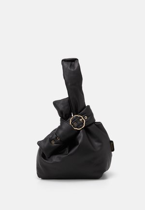 Sac à main en cuir noir avec forme souple et froncée, boucle ronde en or sur la sangle, et poignée de poignet s'étendant vers le haut sur un fond uni.