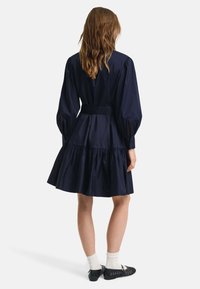 Rochie din bumbac bleumarin cu un corset ajustat și o fustă voluminoasă cu pliuri, având manșete lungi puff și o curea asortată. Material texturat.