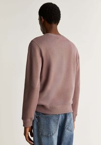 Felpa in mauve neutro, realizzata in tessuto morbido. Collo a giro, maniche lunghe, polsini e orlo a coste, texture liscia, dettagli di cucitura minimi.