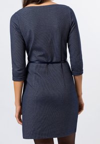 Námořnické pletené šaty s třičtvrtinovými rukávy, upnutým pasem a dvěma bočními kapsami. Hladká textura a jemný geometrický vzor.