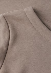 Tessuto beige chiaro con una texture liscia, caratterizzato da un design a V e delicati dettagli di cucitura. Inquadratura ravvicinata di due sezioni sovrapposte.