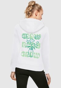 Fehér kapucnis pulóver, zöld virágvázát ábrázoló grafikával és a "GROW" és "BODY" feliratokkal, különböző betűtípusokban a hátsó oldalon. Puha anyag, testhez álló kialakítás.