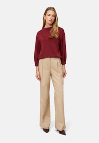 Burgundowa bluzka z długim rękawem i beżowe spodnie z wysokim stanem, materiał o gładkiej fakturze, z dopasowanymi fałdami oraz brązowe szpiczaste obcasy.