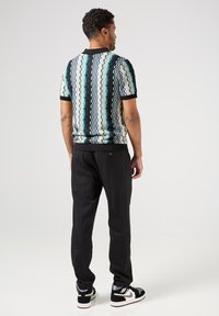 Polo triko s krátkým rukávem a vzorem v tyrkysové, černé a bílé barvě; má žebrovaný límec a manžety, kombinováno s černými kalhotami a teniskami.