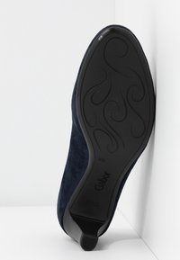 Chaussure en suède marine avec un bout arrondi, un dessus texturé et une semelle en caoutchouc noir lisse ornée de motifs en spirale décoratifs et d'un logo.