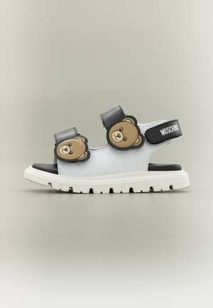 Sandaletto bianco con suola spessa, cinturini neri con facce di orsetto e cinturino alla caviglia nero con il logo Moschino.