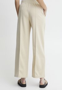 Beige vide bukser med elastisk liv og sidelommer. Blødt stof, lige snit og syede kantdetaljer. Kombinert med flade sandaler.
