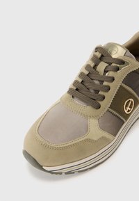 Baskets en daim vert olive et mesh, avec un logo rond doré, des lacets marron, et une semelle rayée blanche et marine. Panneau supérieur texturé.