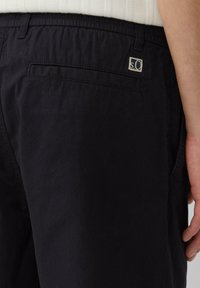 Pantalones negros con cintura elástica, con bolsillos laterales y un bolsillo trasero adornado con un pequeño logotipo. Tela suave y ligera.