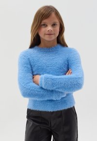 Lichtblauwe, fuzzy trui met lange mouwen en een ronde hals, gecombineerd met zwarte leren broeken. Zachte textuur, aansluitend ontwerp.
