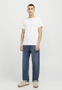 T-shirt en coton blanc, coupe décontractée, associé à un jean en denim bleu, légèrement fuselé ; baskets beiges avec des accents blancs. Détails de bijouterie minimalistes.