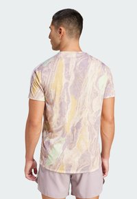 T-Shirt mit kurzen Ärmeln, das ein marmoriertes Muster in lila, gelben und grünen Tönen zeigt. Aus einem weichen, atmungsaktiven Stoff gefertigt.