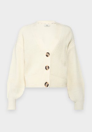 Gilet en tricot crème avec un décolleté en V profond, quatre grands boutons ronds marbrés et des manches bouffantes. Longueur courte avec des poignets et un ourlet côtelés.