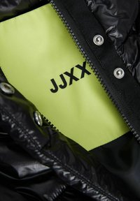 Čierna vypchávaná bunda s lesklým povrchom; vo vnútri má jasne žltú podšívku so vzorom "JJXX" potlačeným čiernou farbou. Obsahuje strieborné detaily.