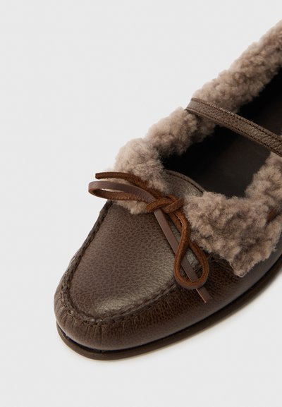 Brown leather shoe with a soft, textured tan fur lining and a decorative tied lace. Rounded toe and stitched detailing along the sole.