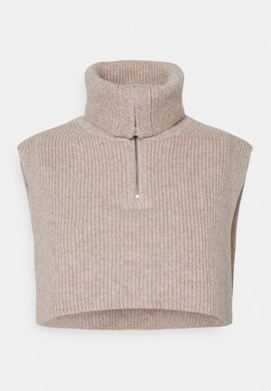 Beige geribbelde gebreide mouwloze trui met een col en een zilveren ritssluiting aan de voorkant, met een iets afgeknipte zoom.
