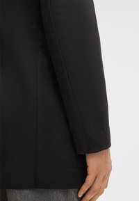 Blazer nero con una texture liscia, vestibilità su misura e maniche lunghe. Caratterizzato da linee pulite e un design strutturato con dettagli di cucitura sottili.