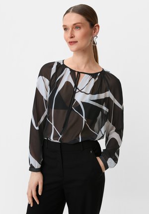 Durchsichtige schwarze Bluse mit weißen und grauen abstrakten Mustern, rundem Halsauschnitt und langen Ärmeln. Kombiniert mit maßgeschneiderten schwarzen Hosen.