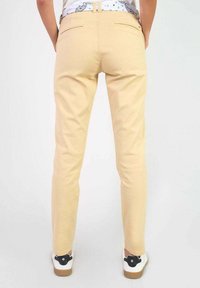 Pantalons en coton jaune clair avec une coupe ajustée, dotés de poches arrière et associés à des chaussures blanches avec des accents noirs.