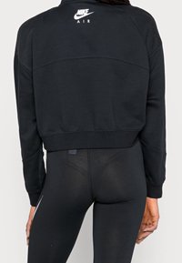 Svart kort sweatshirt med nätaxlar, med Nike Air-logotypen i vitt. Materialet verkar mjukt; designen är sportig och avslappnad.