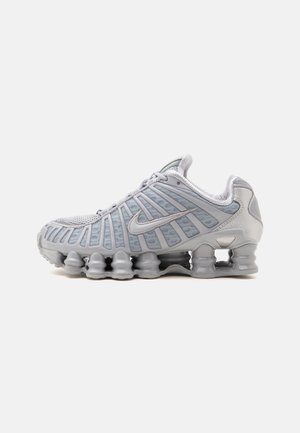Grå Nike løbesko med synlige fjederlignende sålstøtter og mesh-overdel, vist fra siden mod en hvid baggrund.